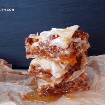 a pile of nut-free vegan baklava on aprchment paper drizzled with syrup.