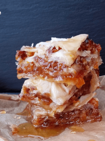 a pile of nut-free vegan baklava on aprchment paper drizzled with syrup.