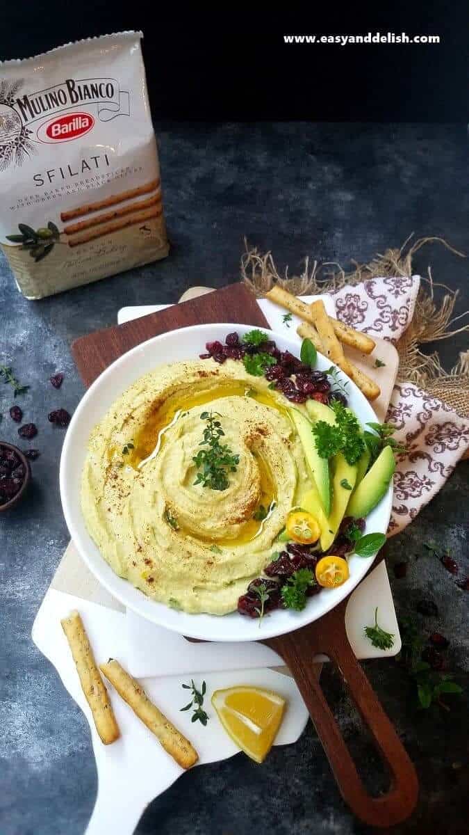 Avocado Hummus Recipe is a no cooking, quick and easy appetizer made with a few simple ingredients, and served with olive breadsticks. It’s perfect for the Holidays! avocado hummus in a bowl with breadsticks on the side