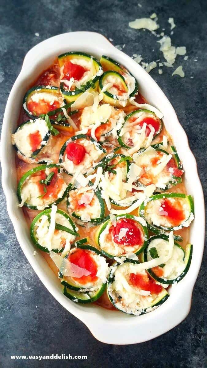 Low carb, naturally gluten-free, and meatless Baked Caprese Zucchini Roll Ups that make dinner a delicious yet easy task. Image of baked caprese zucchini roll ups in a baking dish right before being baked.