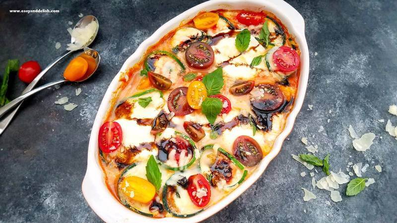 Horizontal image of baked caprese zucchini roll ups after being baked with silverware and vegetables over the table. 