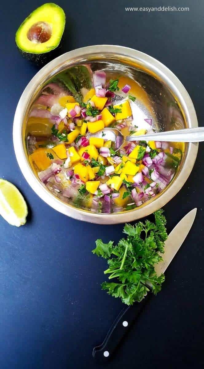  a bowl of mango avocado salsa between some of its ingredients such as lime, cilantro, and avocado