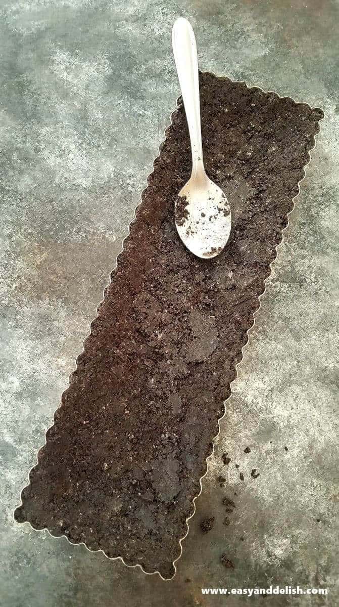 Image of Oreo crust being spooned into the baking pan showing one of the cooking steps