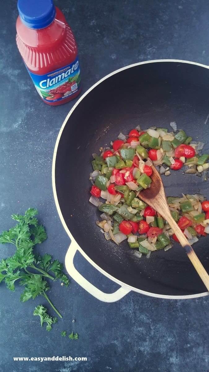 Image showing process of sauteeing vegetables to prepare stew with a bottle of Clamato juice neat the pan. 