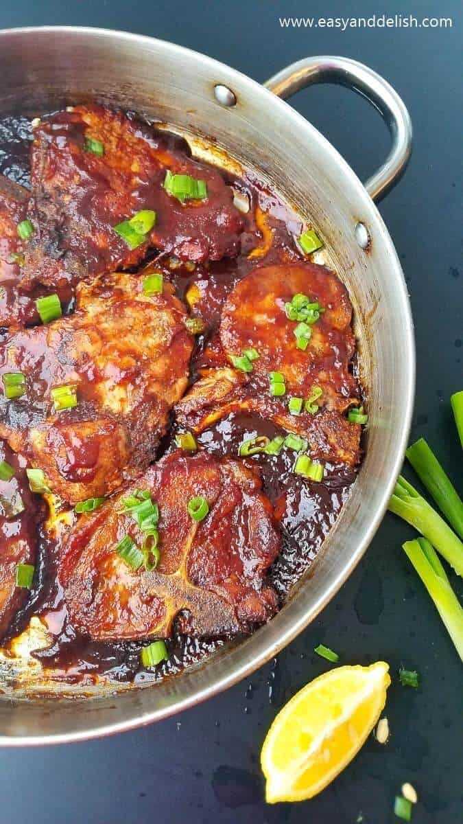 Pan with cooked pan fried barbecue pork chops with lime and green onion near the pan. 