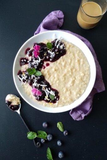 A bowl of coconut oatmeal pudding topped with blueberry sauce