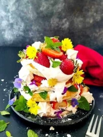 a pile of strawberry pancakes garnished with berries and flowers