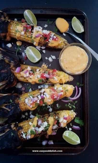 Nacho grilled corn on the cob — featured Four ears of nacho grilled corn on the cob and a bowl of sauce on a baking sheet