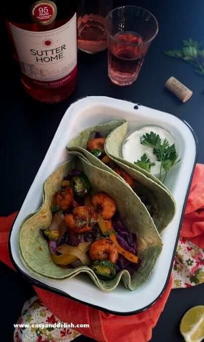 Spicy taco shrimp fajitas served in tortillas with a bottle of wine at the background