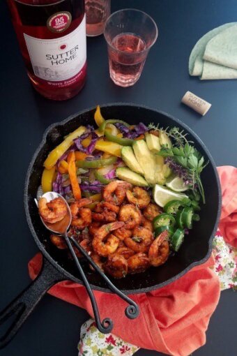 a skillet of shrimp fajitas with wine on the bachground