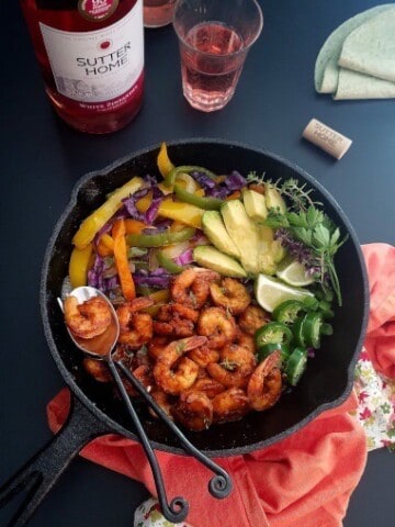 a skillet of shrimp fajitas with wine on the bachground