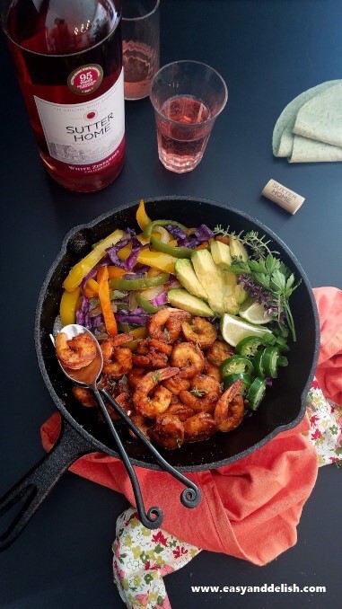 a skillet of shrimp fajitas with wine on the bachground