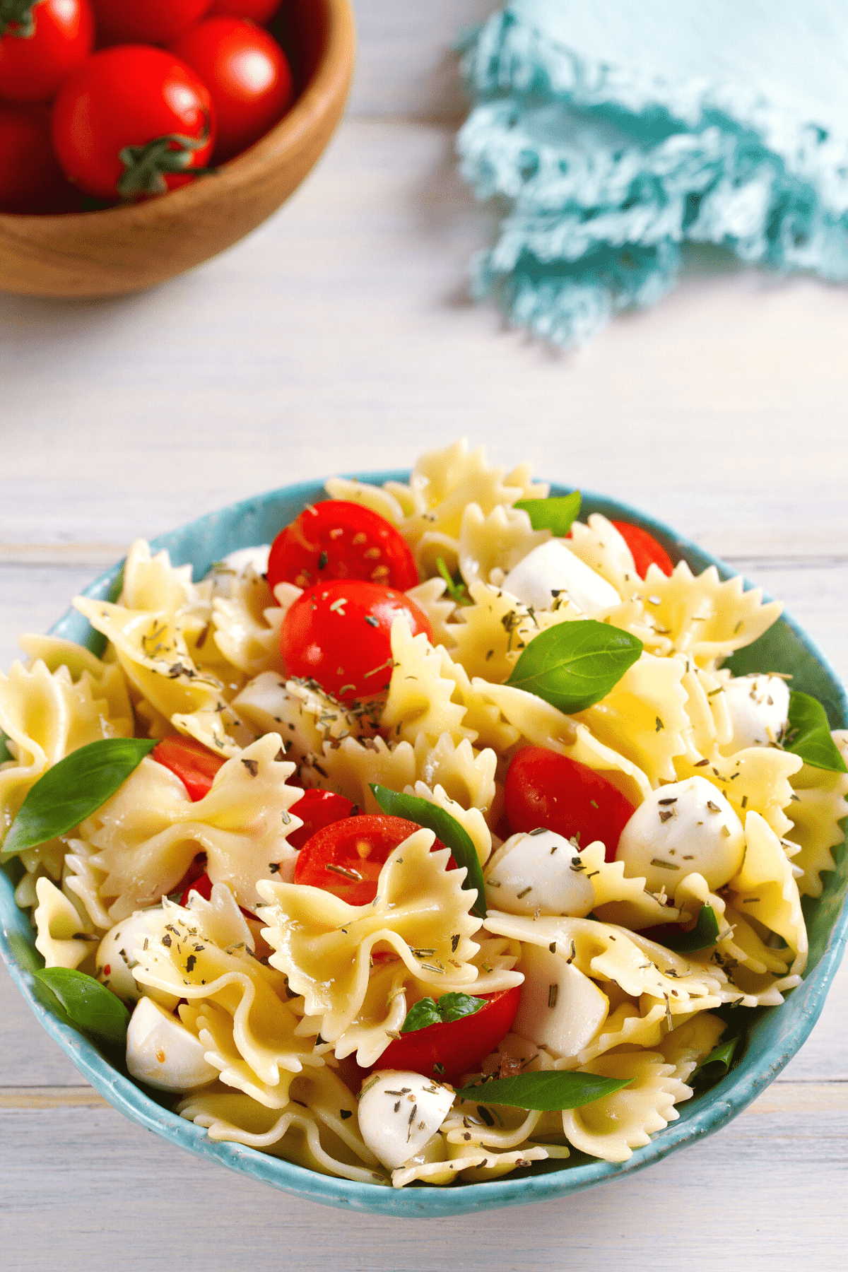 tomato mozzarella pasta salad in a bowl with tomatoes and  napkin on the background. 