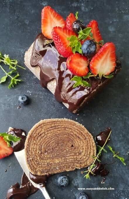 Slices of bolo de rolo cake with spiral alternating cake and fruit filling layers on a board, one slice topped with chocolate sauce and fruit 