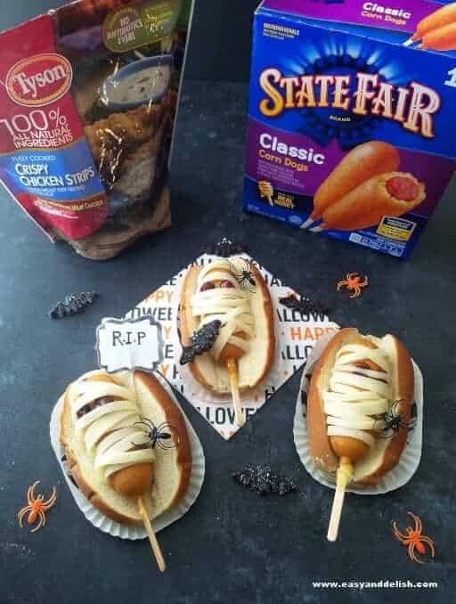 3 mummy coffin corn dogs on table with products on the background