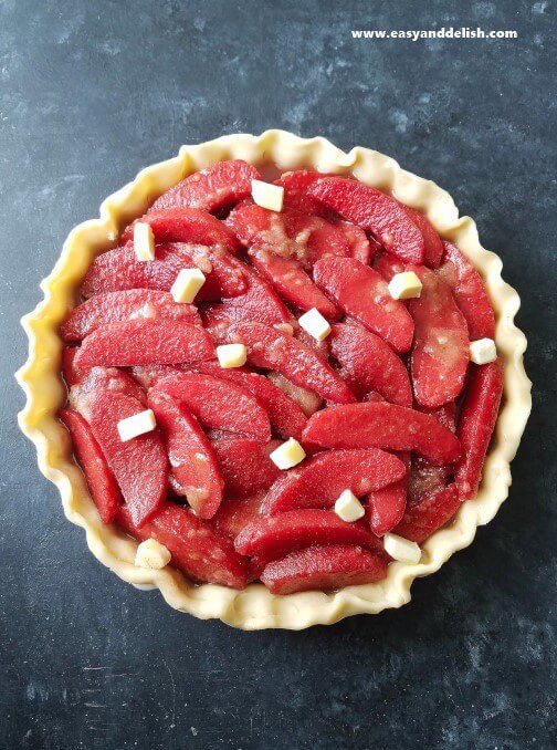 Cooking step for ruby apple pie showing colored apples into pie crust dotted on top with butter