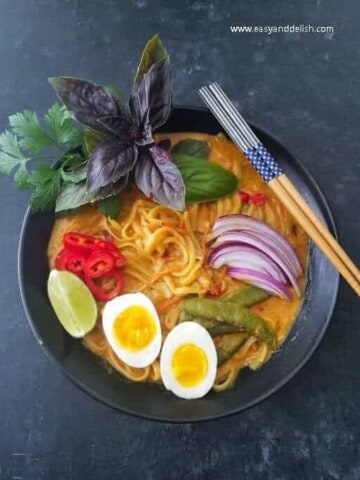 A bowl of coconut noodle soup with chopsticks on the side