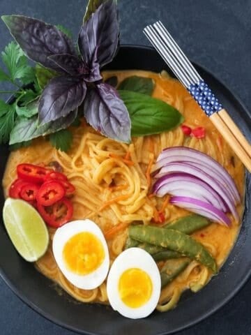 Bowl of creamy noodles with eggs, snap peas, red onion, peppers, lime, and fresh herbs.