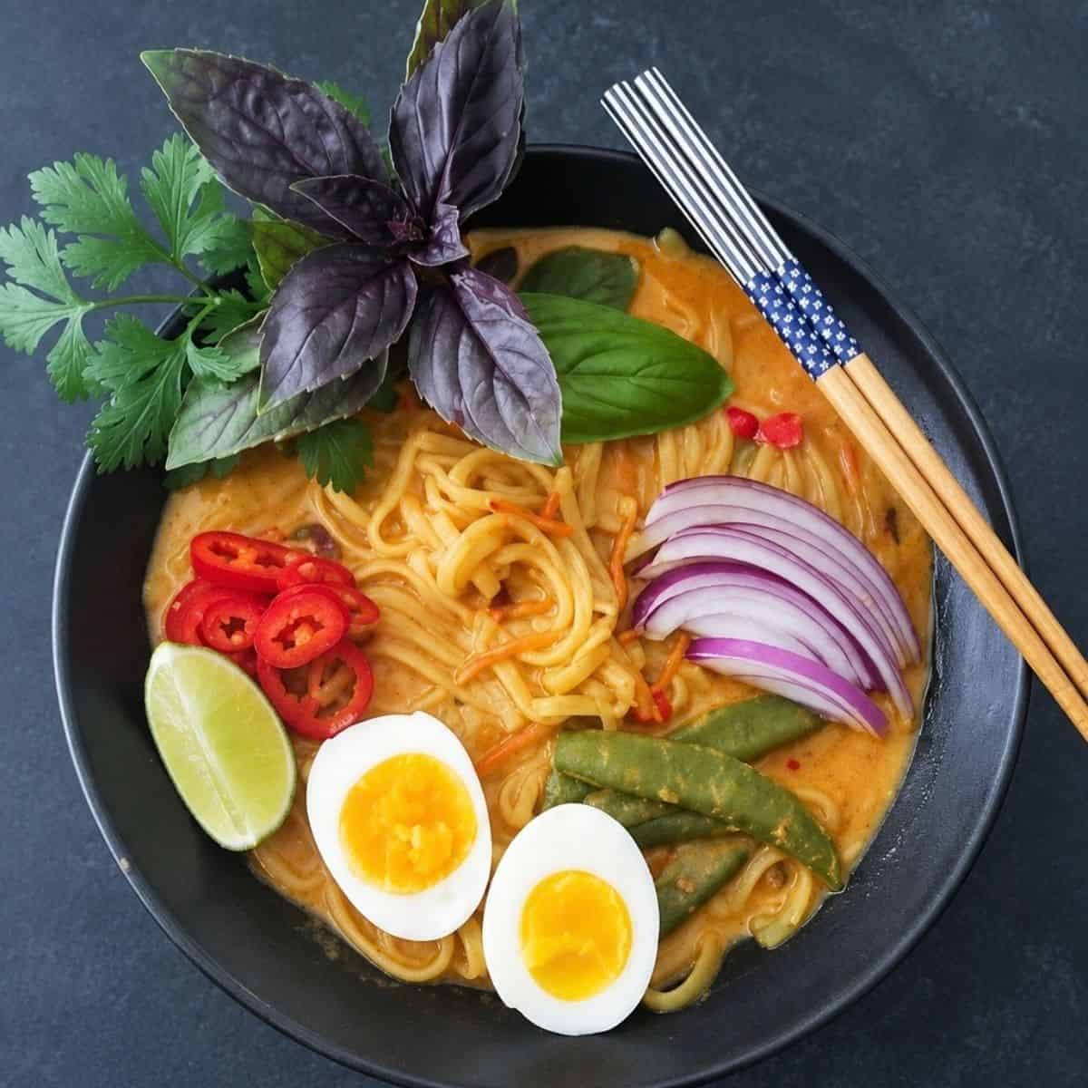 Bowl of creamy noodles with eggs, snap peas, red onion, peppers, lime, and fresh herbs.
