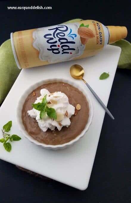 Non-dairy almond caramel pudding on a table with whipped topping can behind