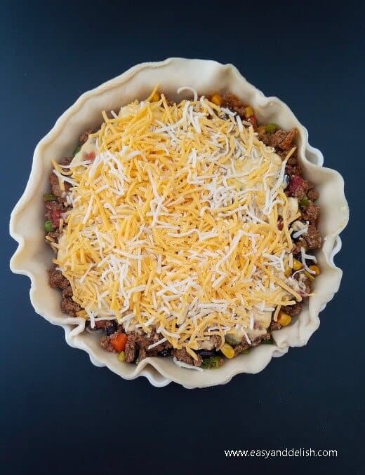 Layering shredded cheese over open chili bean turkey pot pie