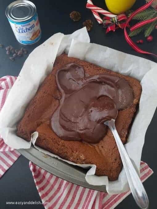 spreading chocolate ganache over baked gingerbread cookie bars