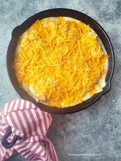 layering baked cod in cheese sauce with shredded cheese