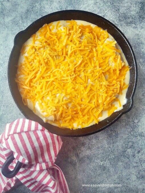 Layering baked cod in cheese sauce with shredded cheese.