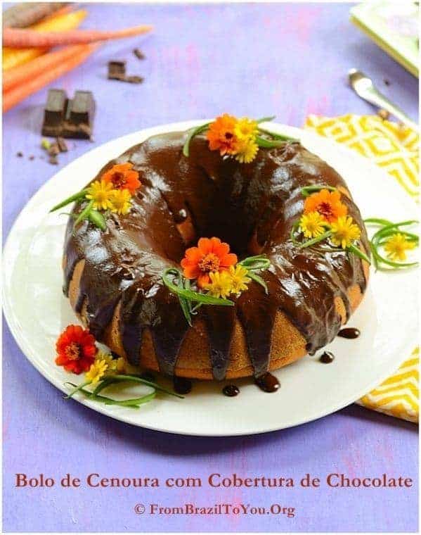 Brazilian carrot cake drizzled with chocolate icing on a white plate and decorated with edible flowers 