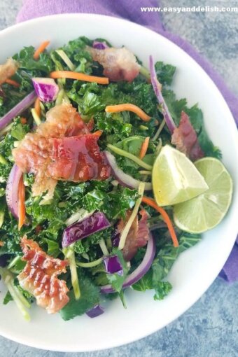 a plate of homemade coleslaw with bacon slices on top and lime wedges