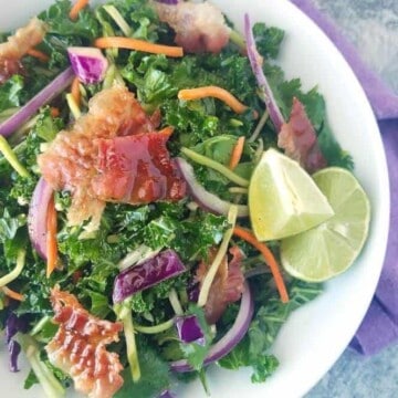 a plate of homemade coleslaw with bacon slices on top and lime wedges