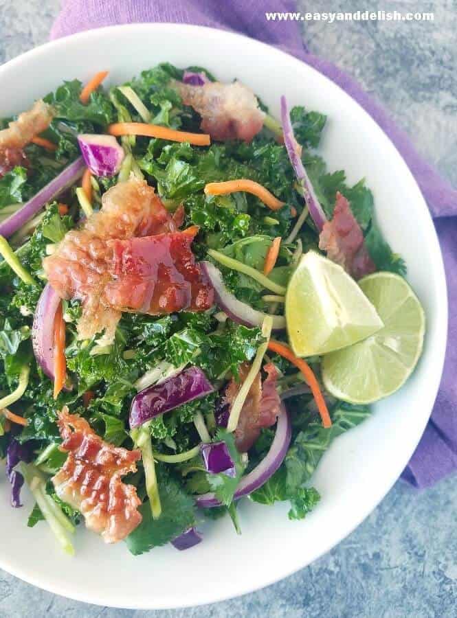 a plate of homemade coleslaw with bacon slices on top and lime wedges