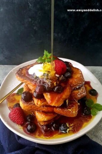 a plate with French toast piled up with a pouring of maple syrup