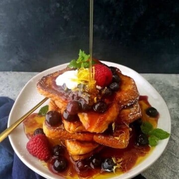 a plate with French toast piled up with a pouring of maple syrup