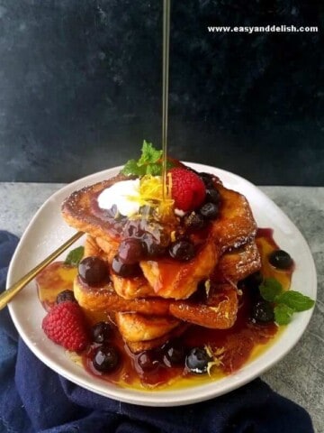 a plate with French toast piled up with a pouring of maple syrup