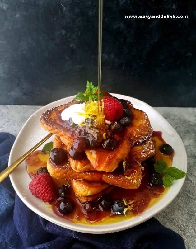 a plate with French toast piled up with a pouring of maple syrup