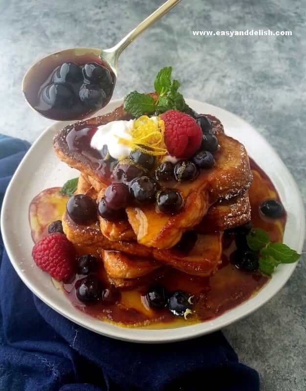 Blueberry compote being poured over French toast stack
