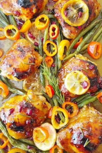 A close up of baked honey mustard chicken thighs with vegetables in a sheet pan.