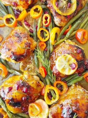A close up of baked honey mustard chicken thighs with vegetables in a sheet pan.