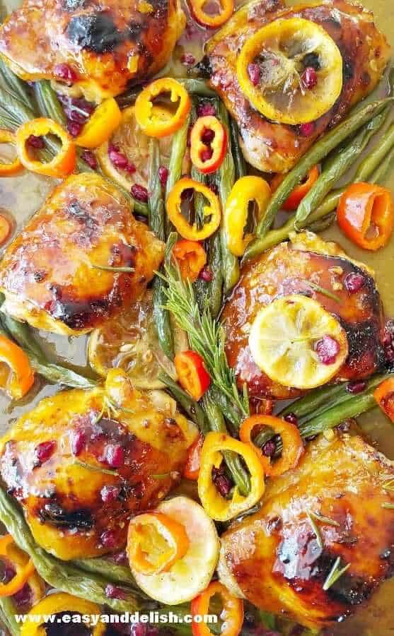 A close up of baked honey mustard chicken thighs with vegetables in a sheet pan. 