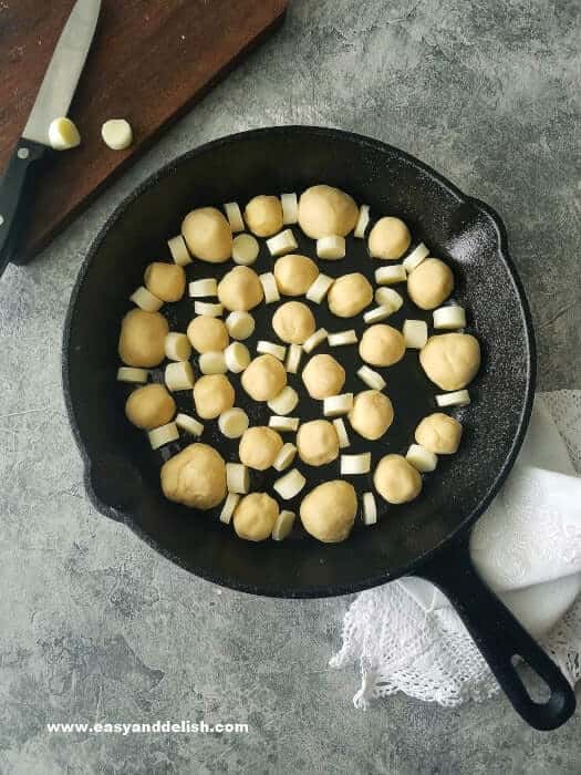 garlic bread rolls arranged in a skillet with cheese before baking