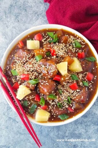 A bowl of sweet and sour pork made in the pressure cooker and chopsticks on the side