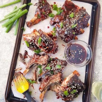 Chinese barbecue ribs in a baking sheet with green onions of the side and top
