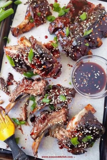 A baking sheet with Chinese barbecue ribs made in the crockpot with a bowl of sauce on the side