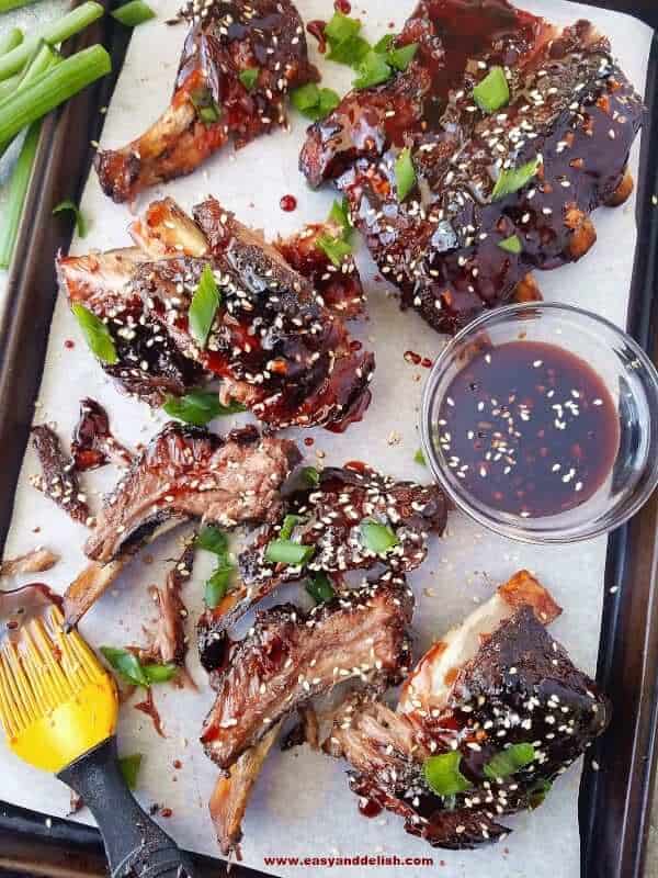 A baking sheet with Chinese barbecue ribs made in the crockpot with a bowl of sauce on the side
