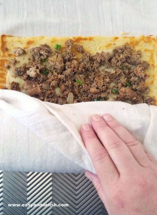 a hand rolling a potato and meat roll