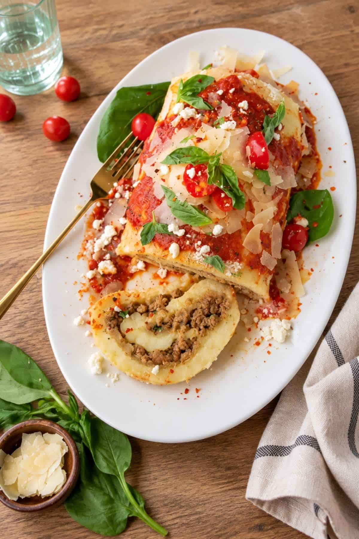 Sliced potato roll filled with ground beef and melted cheese beside the remaining roll topped with tomato sauce and basil.