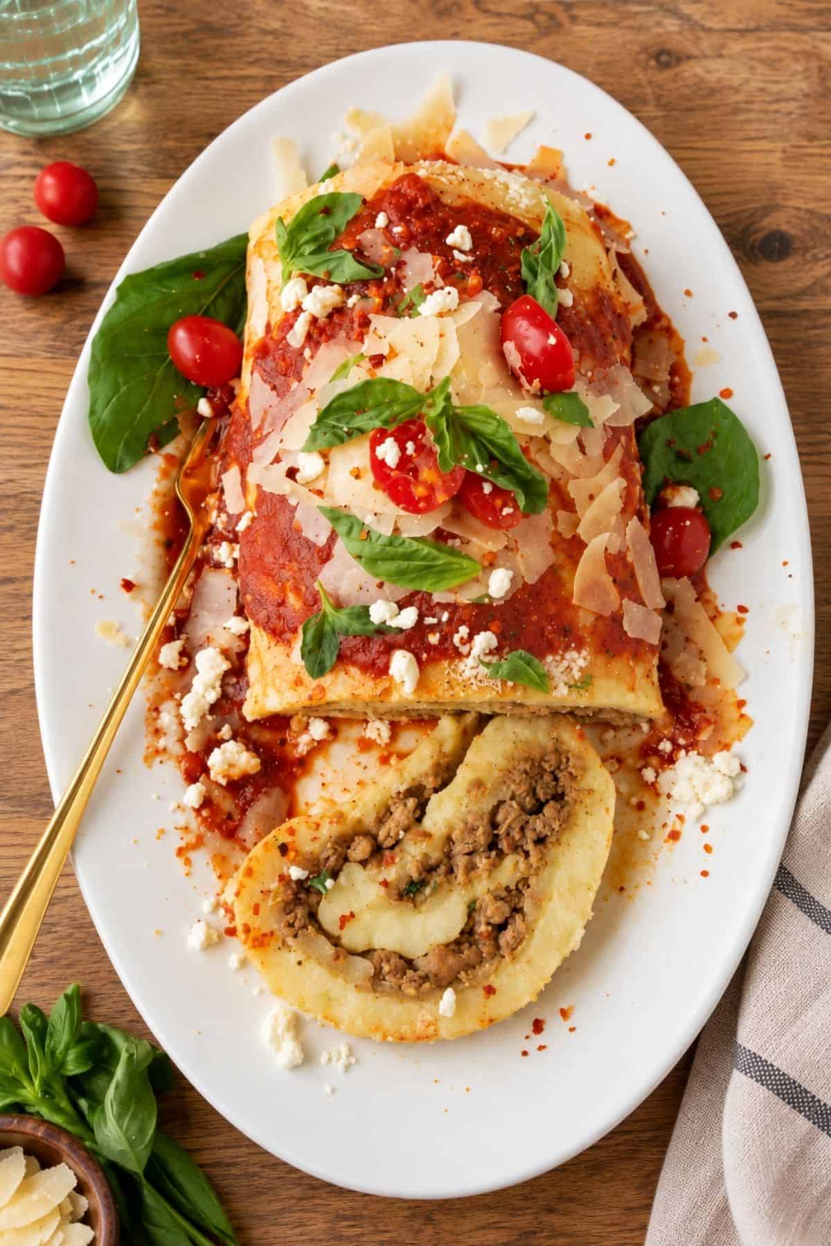 Sliced potato roll filled with ground beef and melted cheese beside the remaining roll topped with tomato sauce and basil.