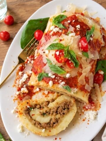 Potato roulade on a white platter with tomato sauce, Parmesan, basil, and a slice filled with beef and cheese.