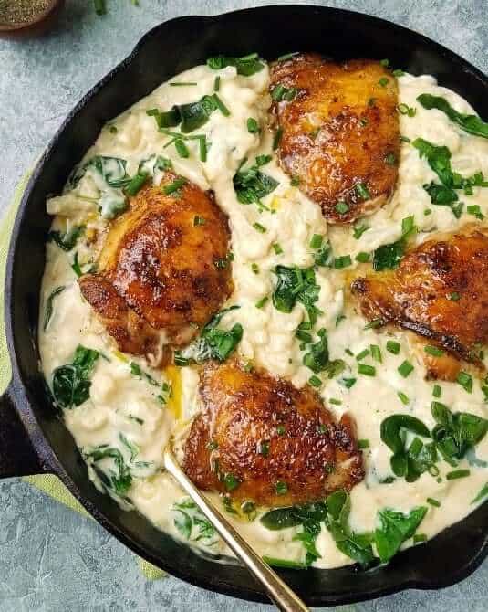 close up of a skillet of cauliflower mac and cheese with chicken thighs